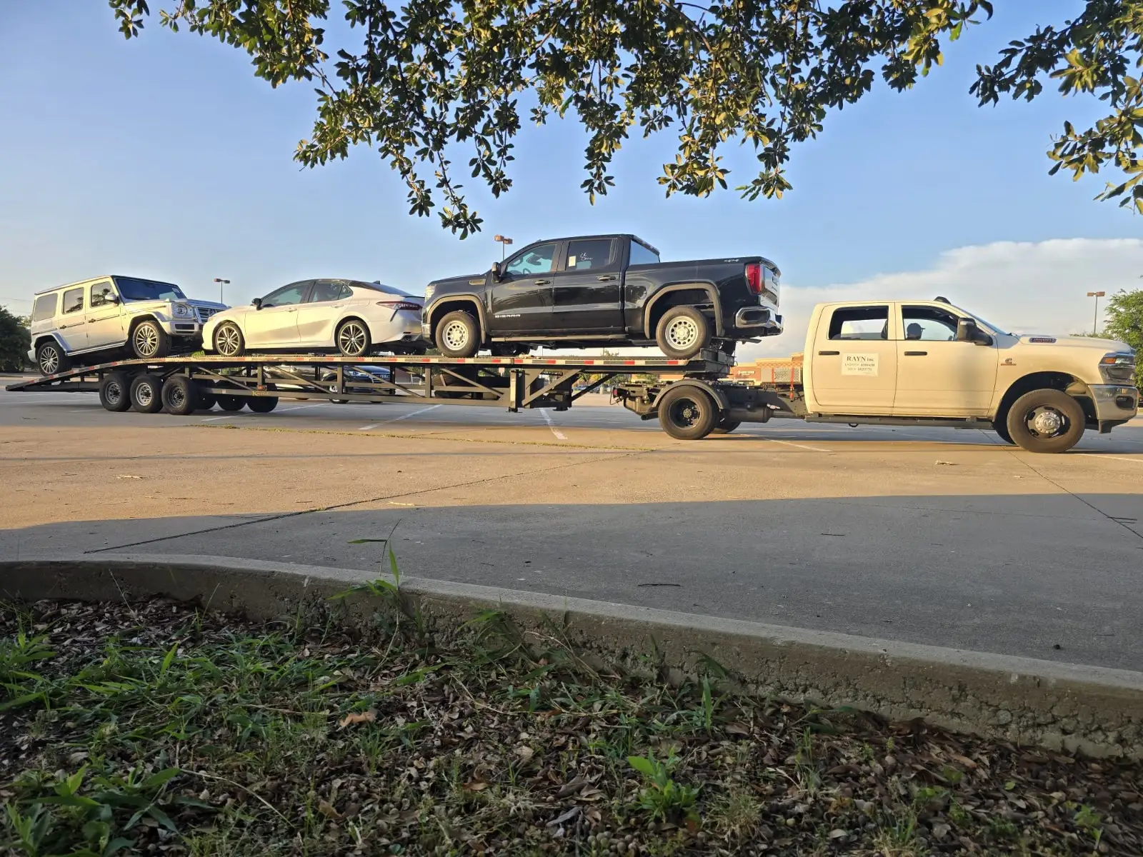 White Ram 3500 dually pulling an open wedge trailer loaded with a Mercedes G-Class, a Toyota Camry, and a GMC Sierra