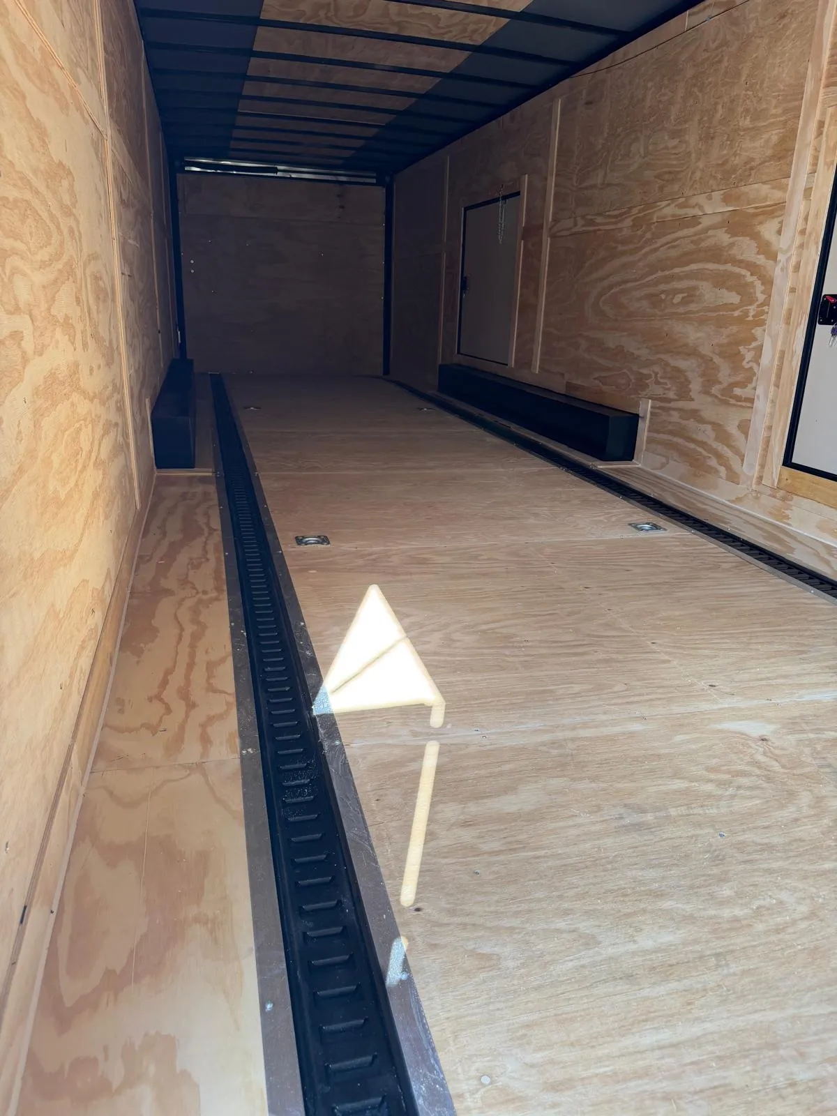 Inside the enclosed trailer, showing plywood walls and the floor E-track tie-down channel